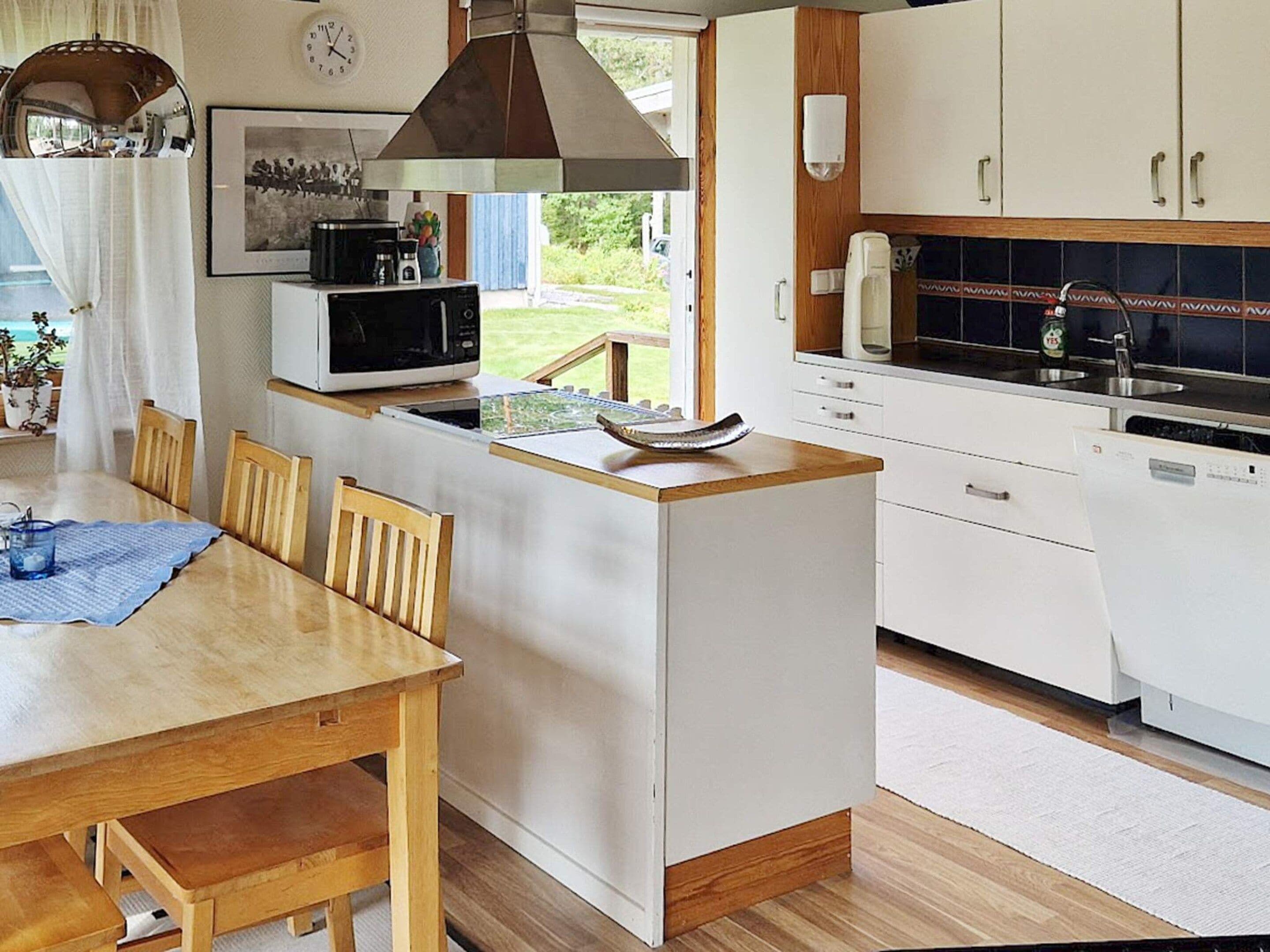 Een kleine keuken met een eethoek, een magnetron, een spoelbak en een klok aan de muur.