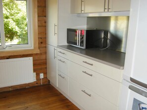A kitchen with white cabinets, a microwave, and a window with a view of trees.