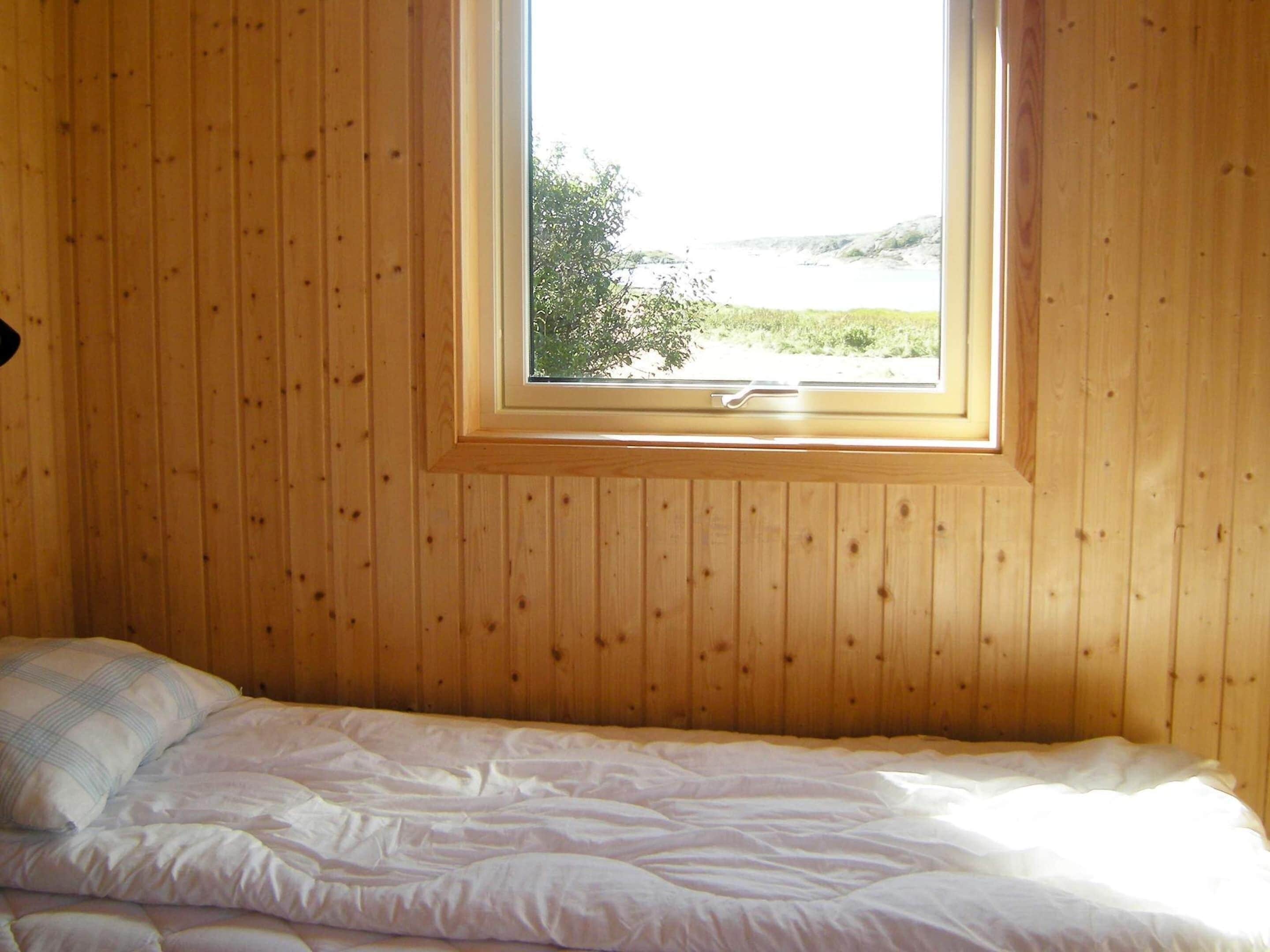 Une chambre avec un lit simple, des murs en bois et une fenêtre donnant sur un paysage verdoyant et un plan d’eau.
