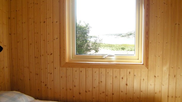 A room with a single bed, wooden walls, and a window with a view of greenery and water. - Holiday Home in HÃ¤lleviksstrand (Hälleviksstrand)
