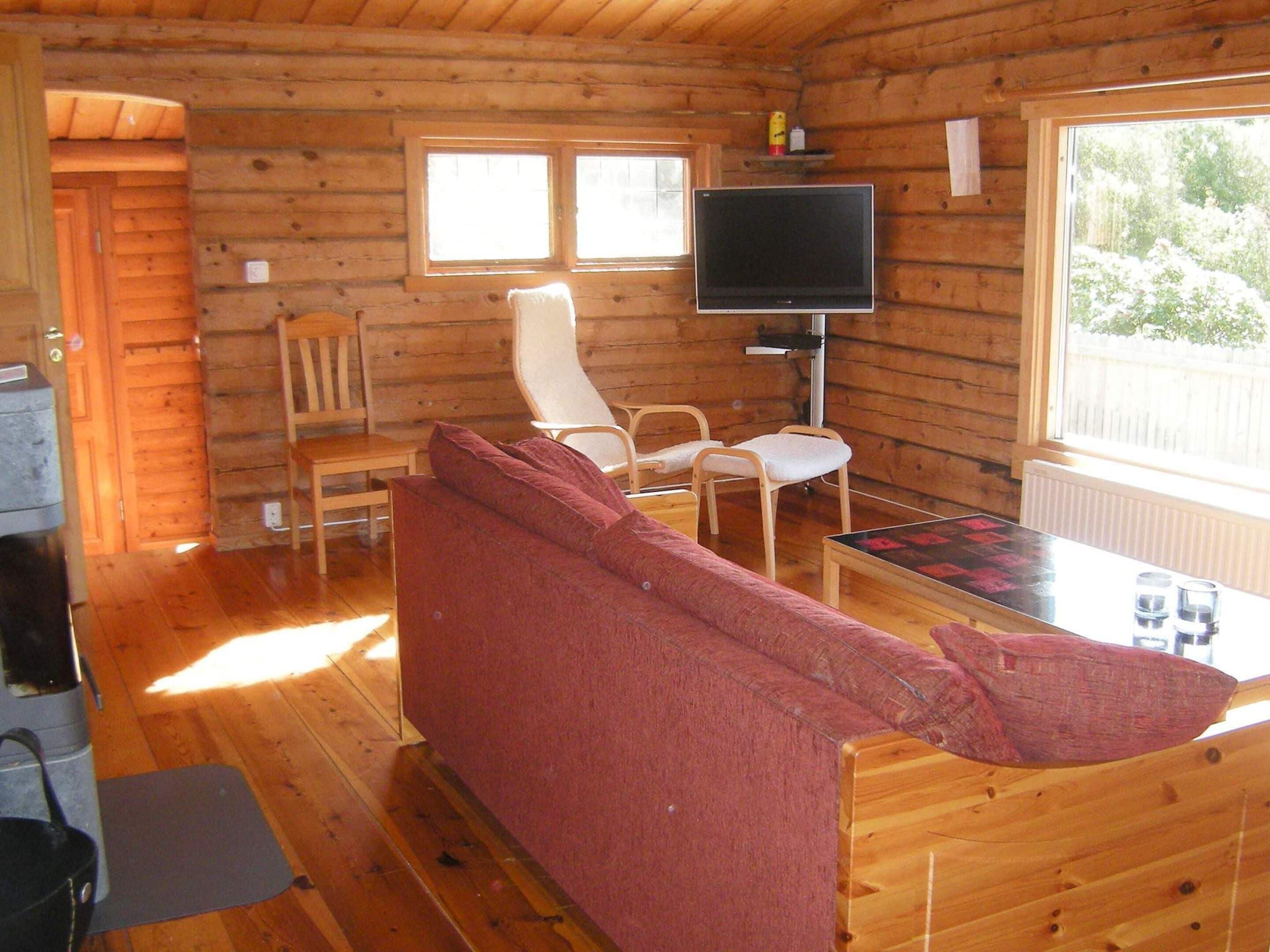 A cozy cabin interior with a sofa, two chairs, a table, a television, and a window.