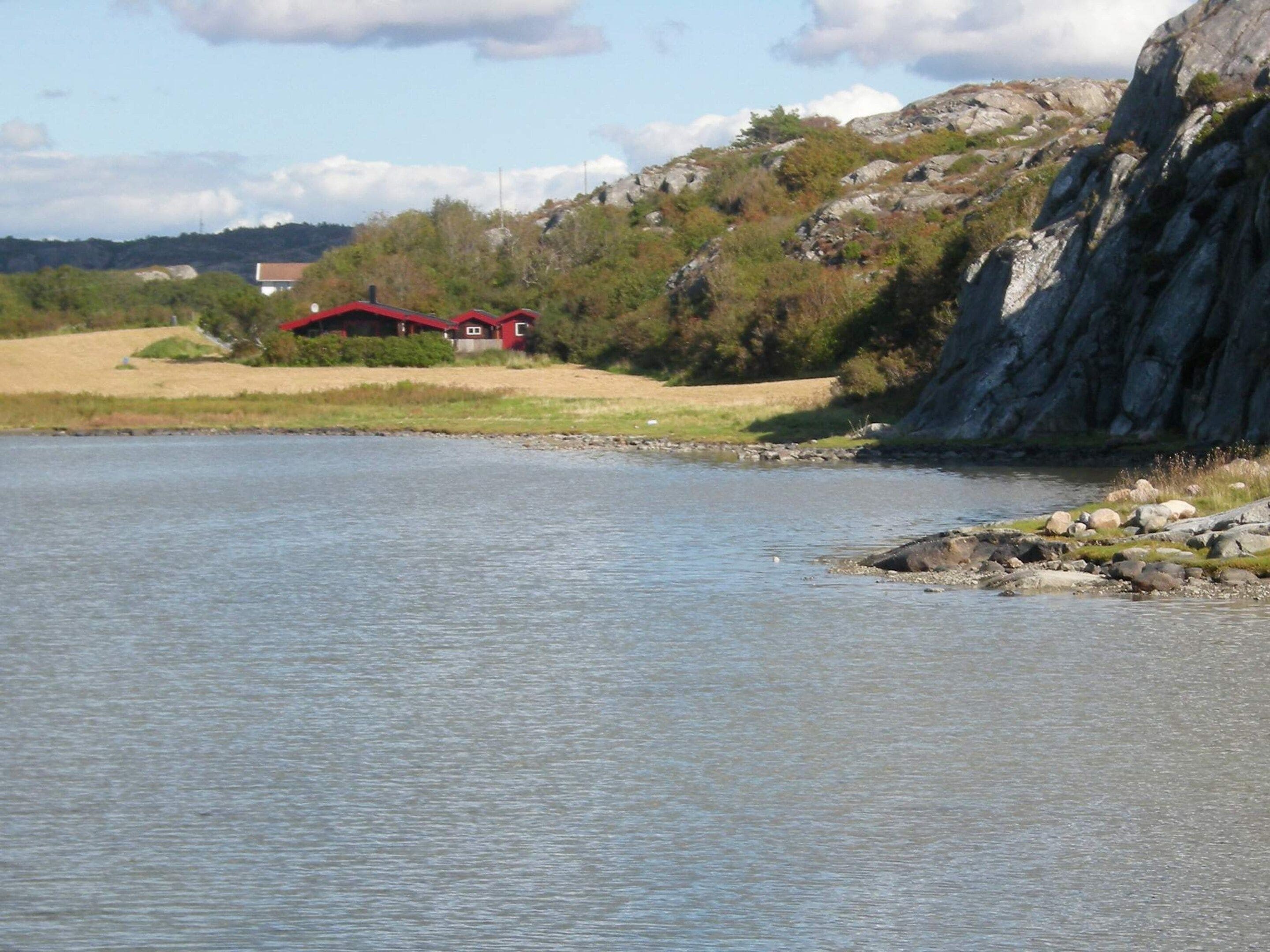 Un lac paisible, avec un bâtiment à toit rouge sur la rive et une colline rocheuse en arrière-plan.