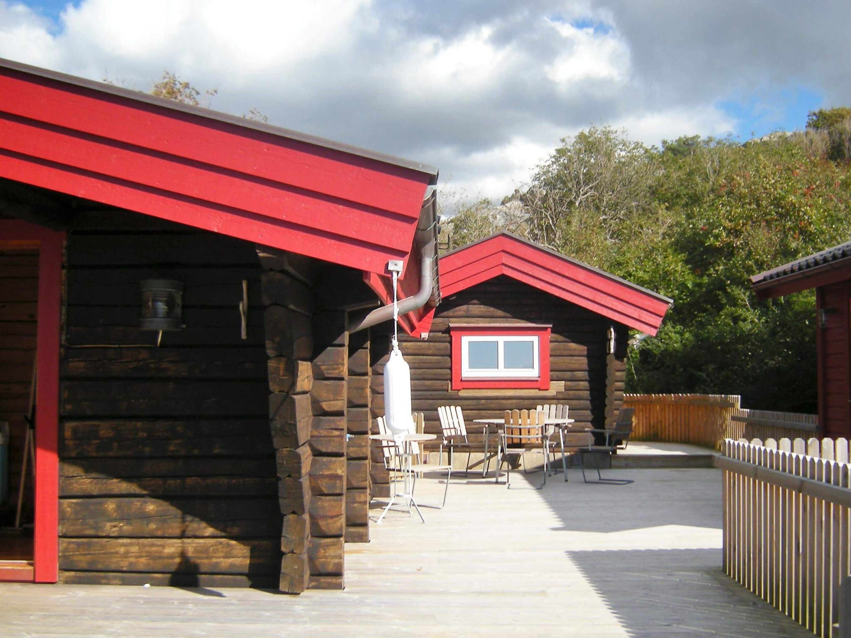 Une cabane en bois avec un toit rouge, une fenêtre et une terrasse avec des chaises.