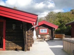 A wooden cabin with a red roof, a window, and a deck area with chairs. - Holiday Home in HÃ¤lleviksstrand (Hälleviksstrand)