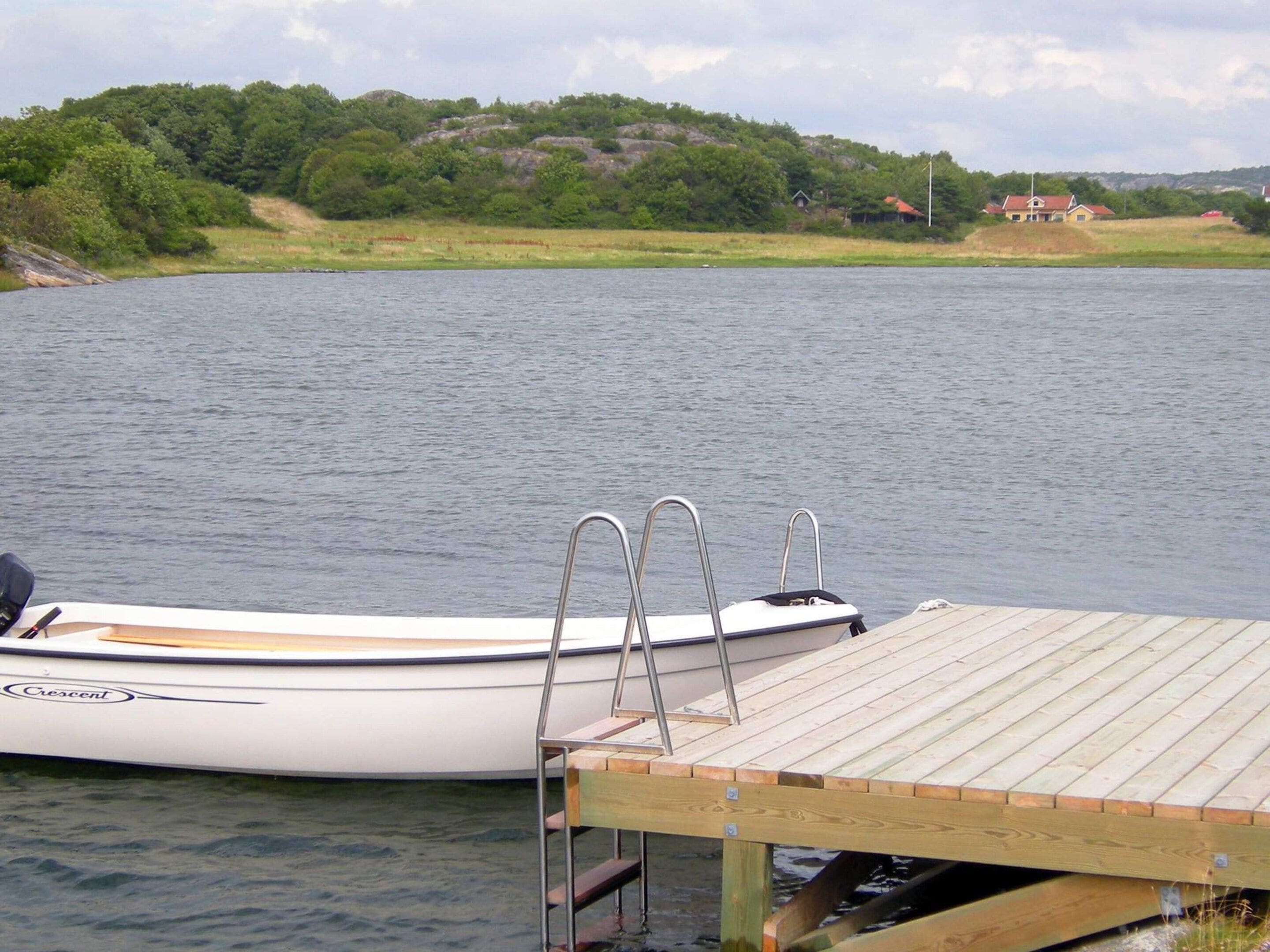 A boat docked at a wooden pier with a view of a forested hillside in the background.