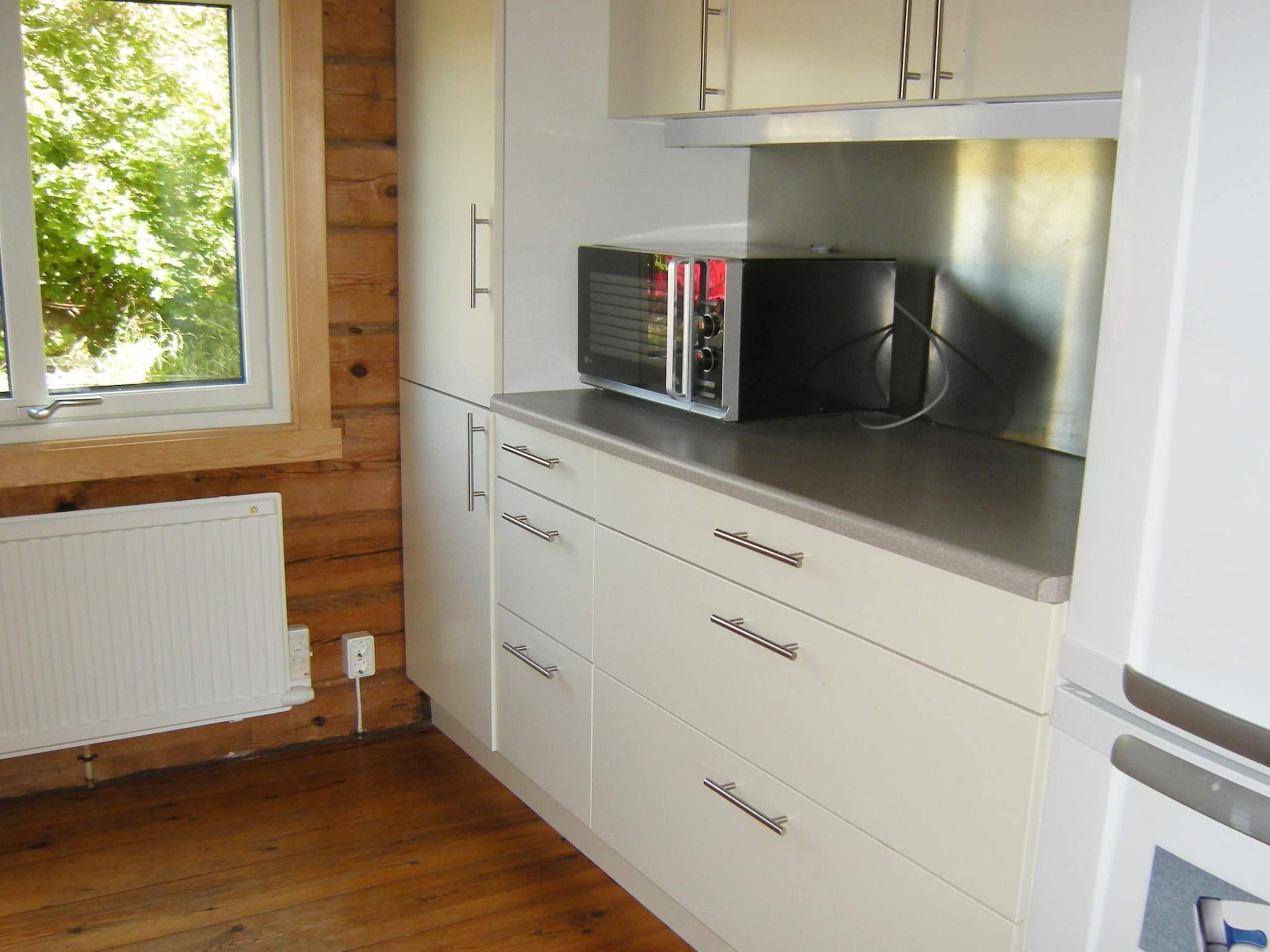 A kitchen with white cabinets, a microwave, and a window with a view of trees.