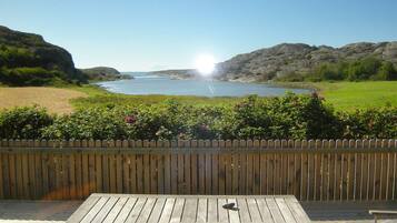 A wooden deck with a table and chairs, overlooking a body of water and rocky landscape.