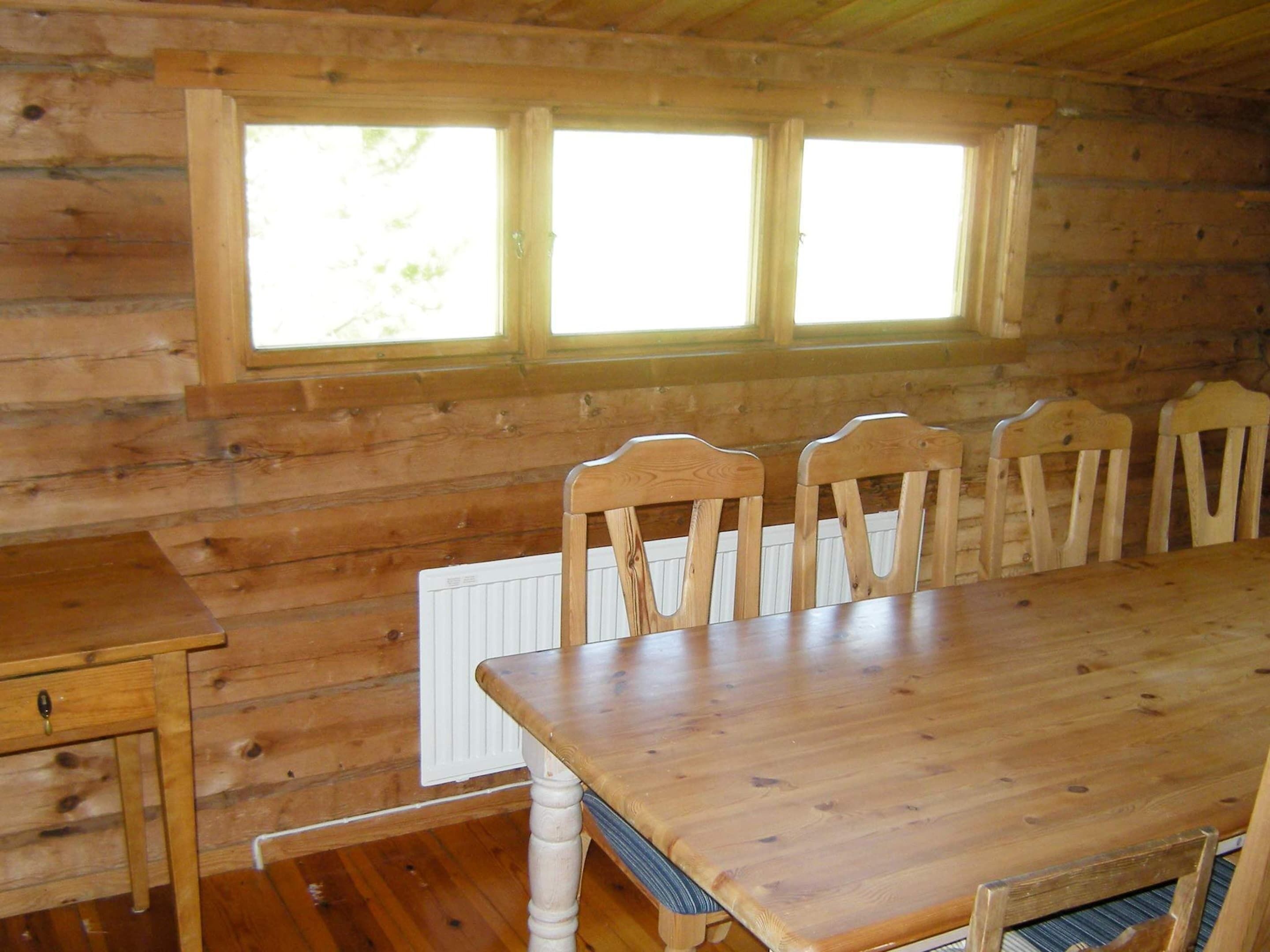 A wooden interior with a dining table and chairs, a window, and a radiator.