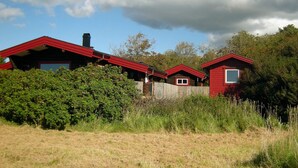 A row of red cabins with a wooden fence in front, surrounded by greenery and under a partly cloudy sky. - Holiday Home in HÃ¤lleviksstrand (Hälleviksstrand)