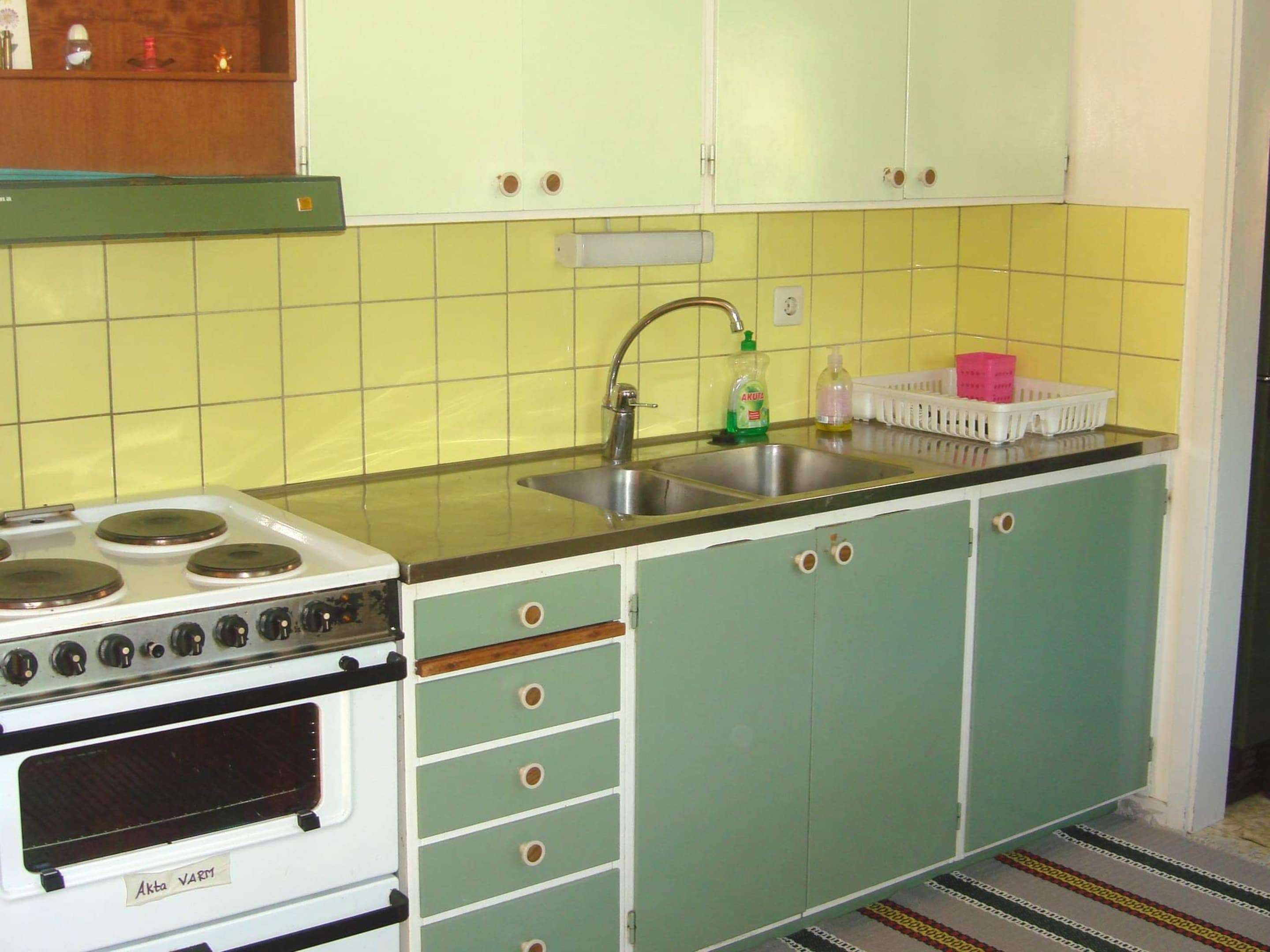 A kitchen with a stove, sink, and green cabinets.