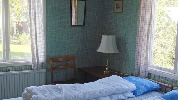 A bedroom with a bed, a chair, a table, a lamp, and a window with curtains.