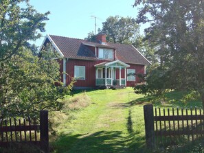 Uma casa de dois andares com varanda, chaminé e quintal cercado.