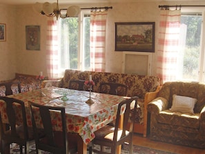 A dining area with a table set for four, surrounded by floral-patterned chairs. A sofa and armchairs are positioned against the wall, and a painting is displayed above a window. - 6 Person Holiday Home in Morlunda (Mörlunda)