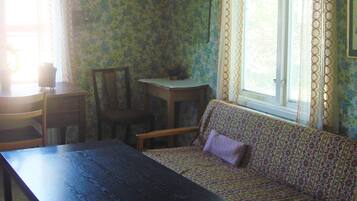 A room with a patterned sofa, a wooden table, a chair, and a window with curtains.