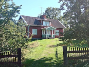 A red house with a porch and a chimney, surrounded by trees and a grassy yard. - 6 Person Holiday Home in Morlunda (Mörlunda)