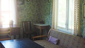 A room with a patterned sofa, a wooden table, a chair, and a window with curtains.