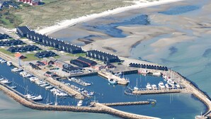 An aerial view of a coastal marina with boats docked, a pier, and a row of houses in the background.