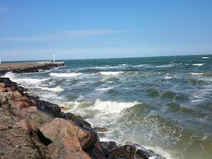 A rocky shoreline with waves crashing against it, a pier extending into the water, and a lighthouse in the distance. - Spacious Villa near Beach in Hadsund (Hadsund)