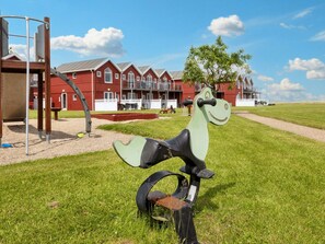 A playground with a green and black bicycle sculpture, a red building with multiple windows, and a clear sky.