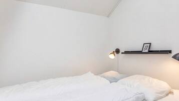En enkeltseng med hvide sengetøj i et rum med hvide vægge og en loftlampe.