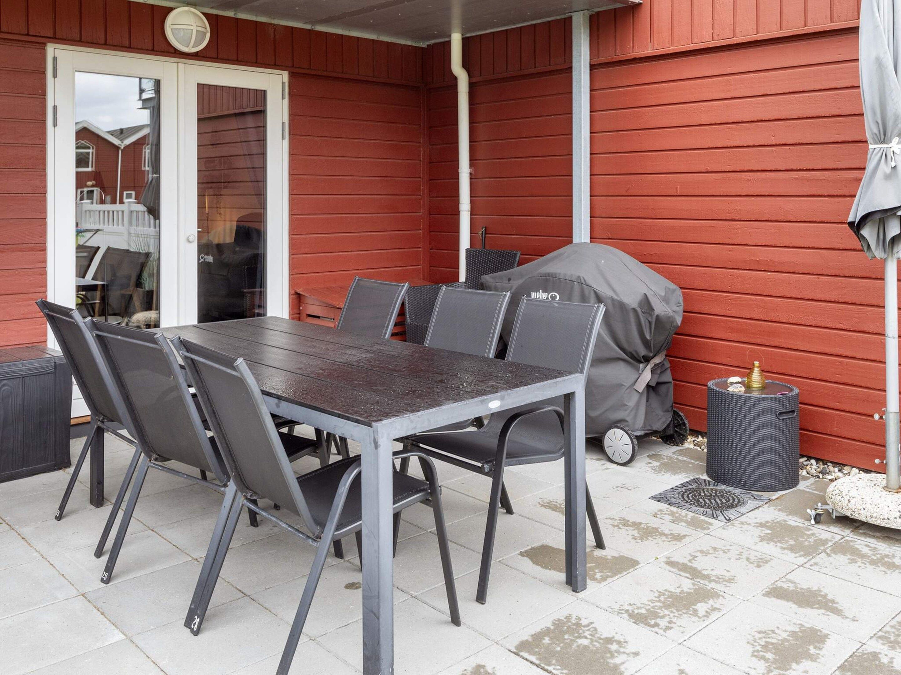 A covered patio with a table and chairs, a grill, and a trash can.