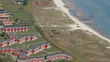 Uma área residencial costeira com casas vermelhas dispostas em fileiras, uma praia de areia e vista clara para o mar.