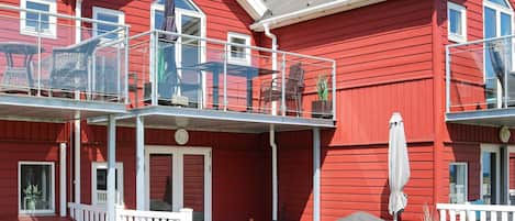 A red building with a balcony, outdoor seating, and a grill.