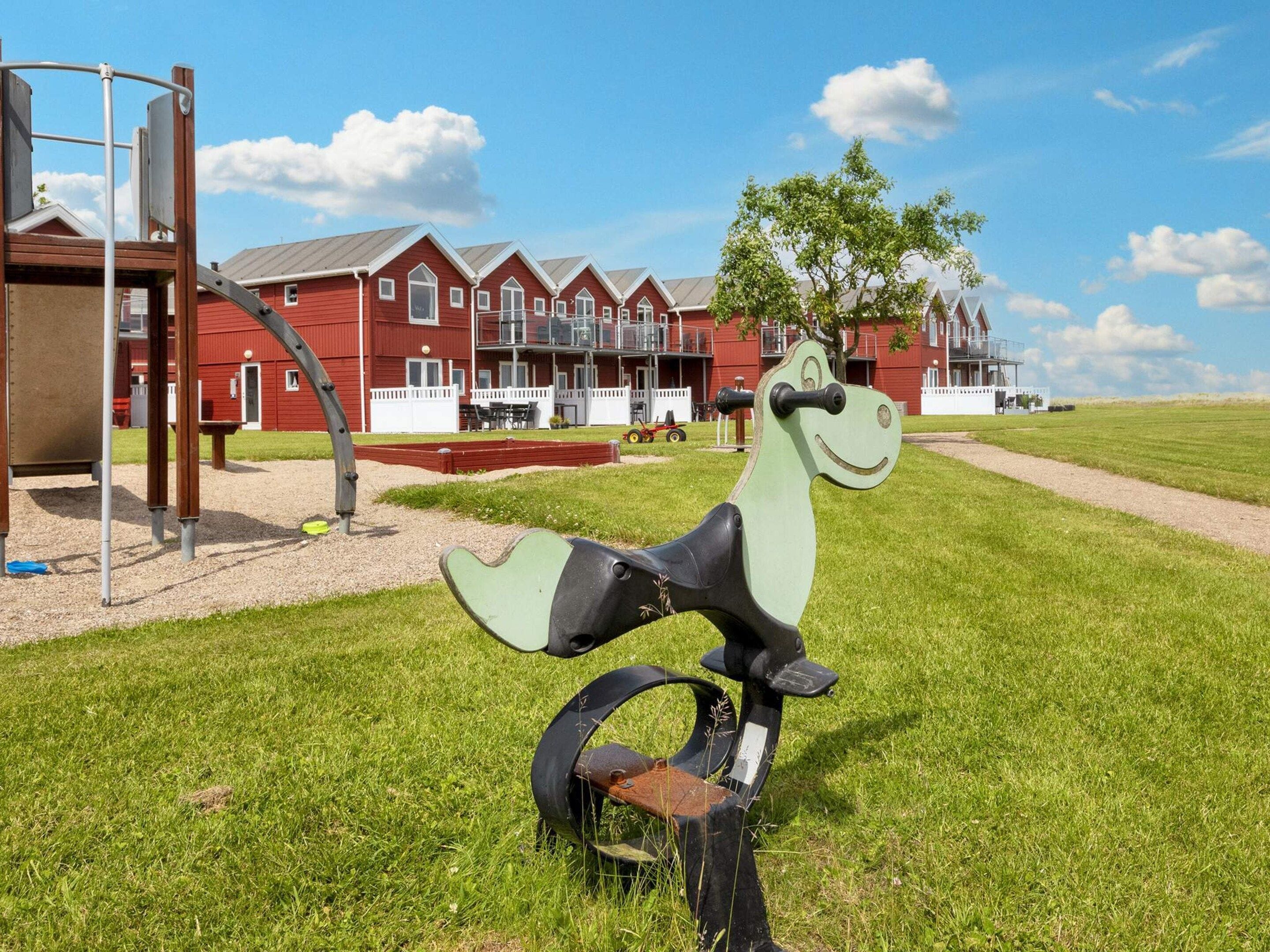 A playground with a green and black bicycle-like structure in a grassy area with a red building in the background.