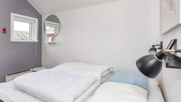 Un dormitorio con cama, lámpara de noche, ventana y espejo.