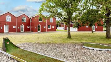 A red building with multiple windows and doors, surrounded by a grassy area with trees and a small green play structure.