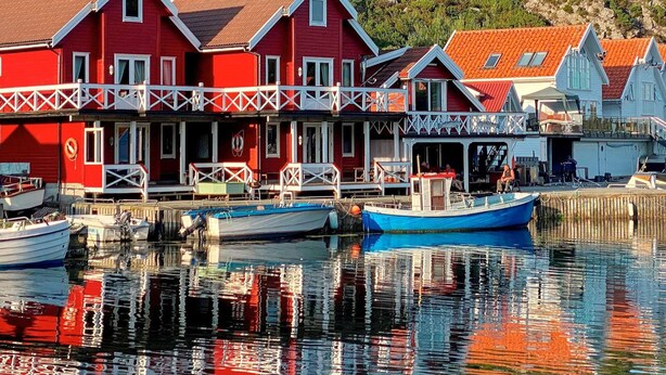 Un edificio frente al agua con fachada roja, varios balcones y un muelle con barcos.