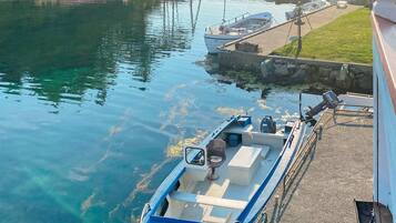 Un barco amarrado en un puerto deportivo, con una vía fluvial despejada, una zona verde con flores y un muro de piedra.