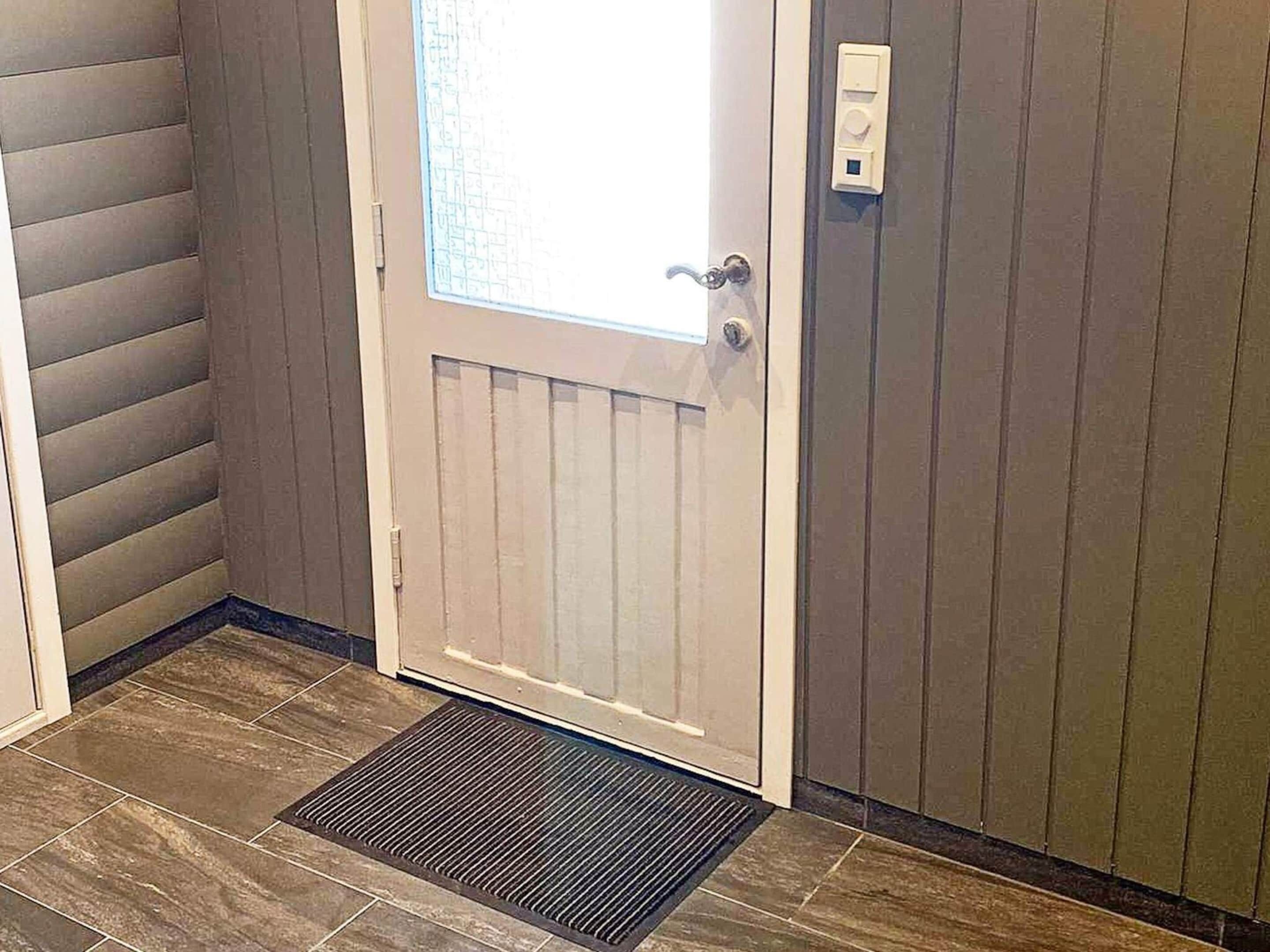 A door with a window, a doorbell, and a mat at the entrance.