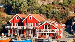 Un edificio rojo con balcón, barcos amarrados y una ladera rocosa al fondo.