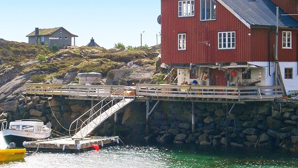A red house with a dock extending into the water, a smaller house in the background, and a rocky hillside. - 6 Person Holiday Home in Ballstad-by Traum (Vestvågøy)