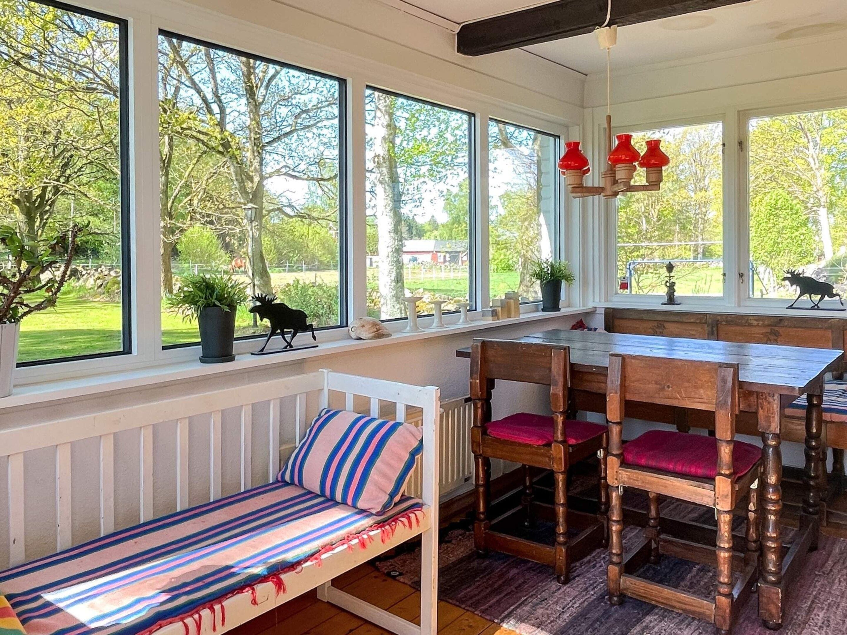 A cozy room with a wooden dining table, a bench with striped cushions, and large windows offering a view of a garden.