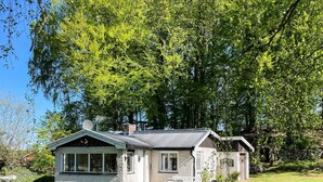 Ein kleines Steinhaus mit geneigtem Dach, großen Fenstern und einer Terrasse mit Gartenmöbeln.