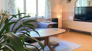 A living room with a sofa, a round table, a television, and a large window with curtains. - 4 Person Holiday Home in Klippan (Klippan)