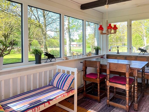 A cozy room with a wooden dining table, a bench with striped cushions, and large windows offering a view of a garden. - 4 Person Holiday Home in Klippan (Klippan)