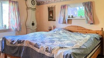 A bedroom with a wooden bed, a clock on the wall, and a window with curtains.