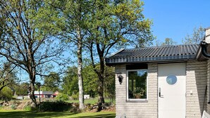 A small stone building with a metal roof, a window with a round glass, and a door with a keypad lock. There is a table and two chairs outside. - 4 Person Holiday Home in Klippan (Klippan)