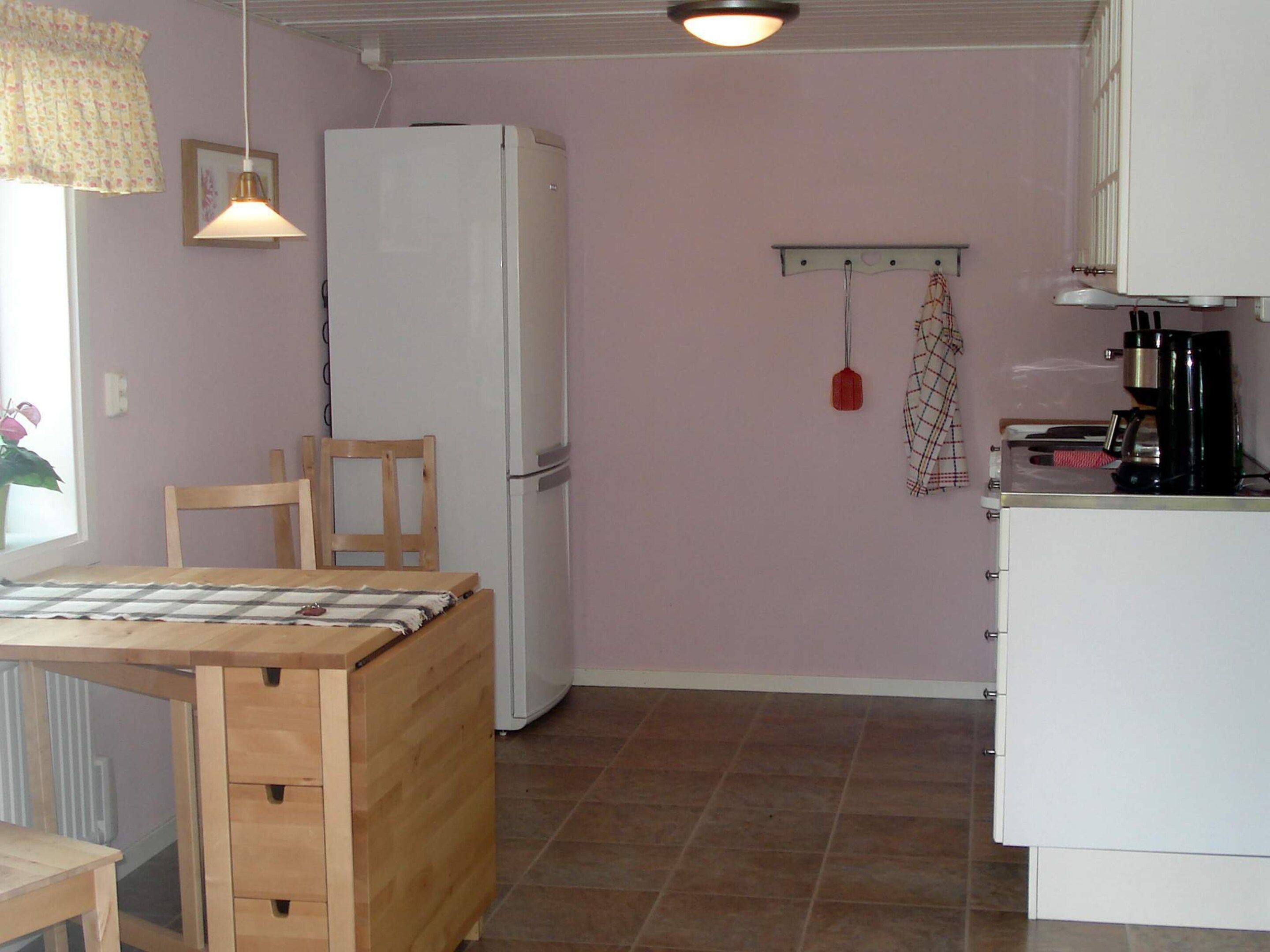 A compact kitchen with a refrigerator, a wooden dining table, and a hanging light fixture.