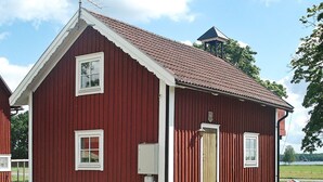 Un bâtiment en bois rouge, doté d’un toit à pignon, d’un petit porche et d’une seule porte.