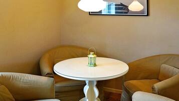 A room with a round table, two chairs, a hanging light fixture, and a framed picture on the wall.