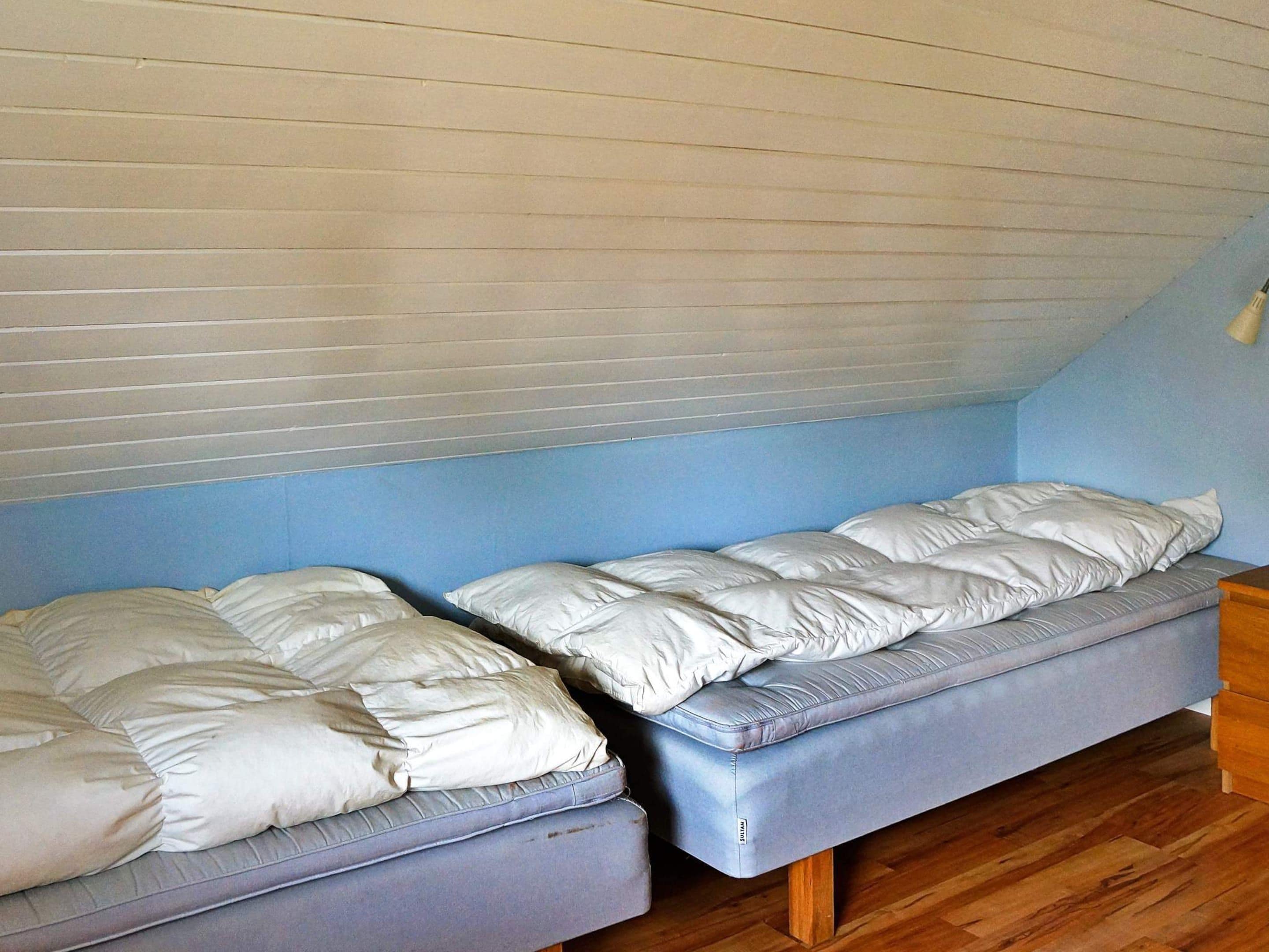 A room with two single beds, wooden flooring, and a sloped ceiling.