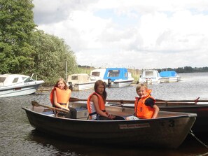 Three people in a small boat with life jackets, docked near a body of water with other boats and a forested area in the background. - 5 Person Holiday Home in Lonashult (Lönashult)