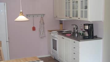 A compact kitchen with white cabinets, a stove, a sink, and a coffee maker.