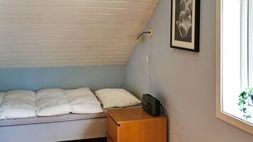A small, single-bed room with a sloped ceiling, a bedside table with a radio, and a framed picture on the wall.