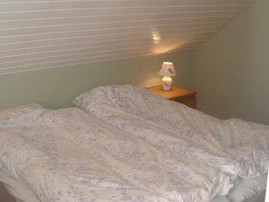 A single bed with a floral-patterned blanket in a room with a sloped ceiling and a nightstand with a lamp. - 5 Person Holiday Home in Lonashult (Lönashult)