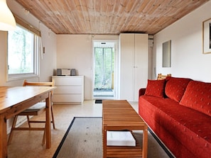 A room with a wooden ceiling, a red sofa, a wooden table, a white cabinet, and a window with a view of greenery. - 2 Person Holiday Home in Tyringe (Tyringe)
